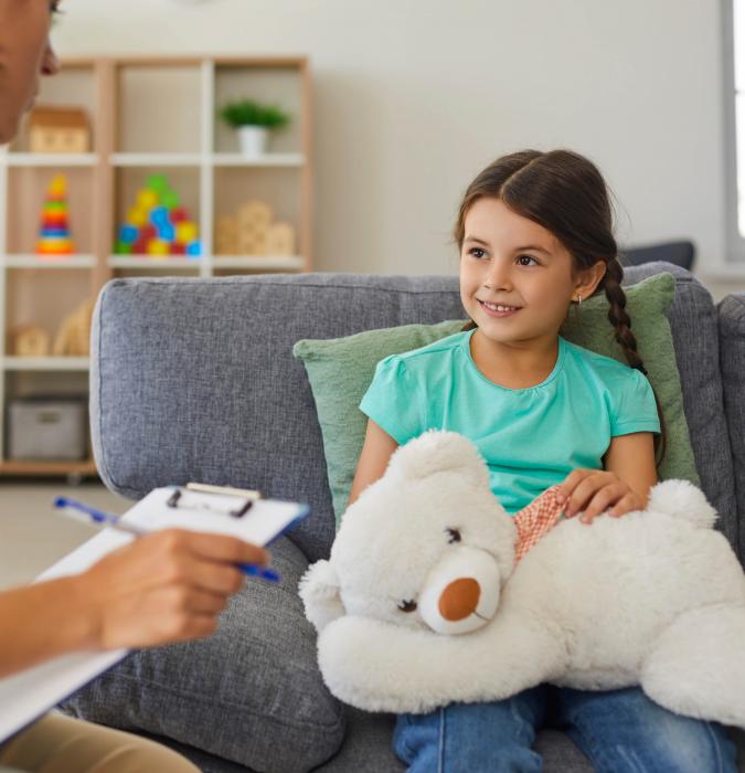 A little girl smiles while her therapist talks to her. 